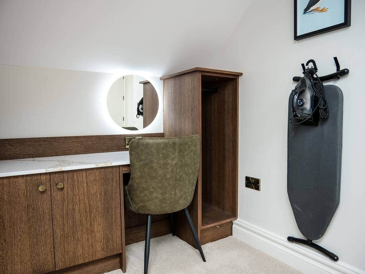 A room with a wooden desk, a green chair, a mirror, and a surfboard on the wall.
