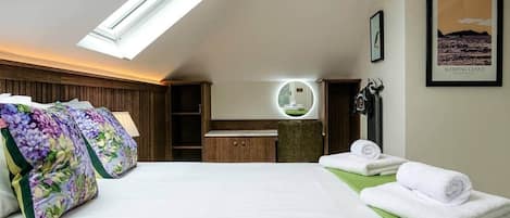 Une chambre d’hôtel avec un puits de lumière, un lit agrémenté d’oreillers à motifs floraux, une coiffeuse avec un miroir et un tableau encadré accroché au mur.