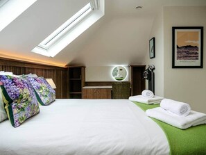 A hotel room with a skylight, a bed with floral pillows, a vanity with a mirror, and a framed picture on the wall.
