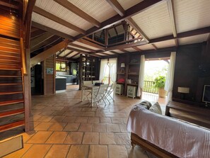 A spacious interior with a stone floor, wooden beams, a dining area, kitchen, and a balcony with a potted plant.