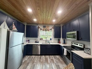 A kitchen with dark cabinets, stainless steel appliances, and a wooden ceiling.