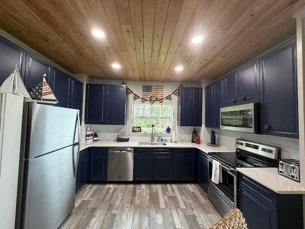 A kitchen with dark cabinets, stainless steel appliances, and a wooden ceiling.