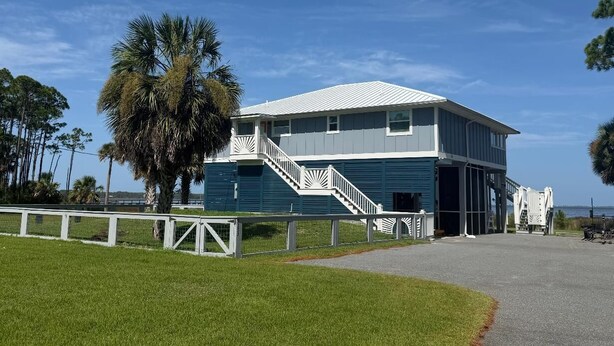 A two-story building with a white staircase, a covered porch, and a view of the ocean.
