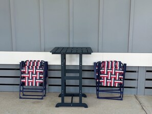 A small outdoor table with two chairs, each with a patterned seat cushion, against a grey wall.