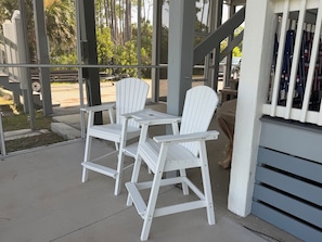 A covered outdoor seating area with two white Adirondack chairs and a small table.