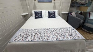 A neatly made bed with a white comforter and pillows, a quilt with a pattern, and a painting of boats on the wall.