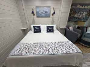 A neatly made bed with a white comforter and pillows, a quilt with a pattern, and a painting of boats on the wall. - Relax on the Bay-Stunning Sunsets & the Perfect Coastal Getaway (Port St. Joe)
