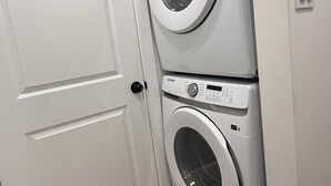 Une buanderie avec deux machines à laver superposées, une porte blanche et un interrupteur sur le mur.