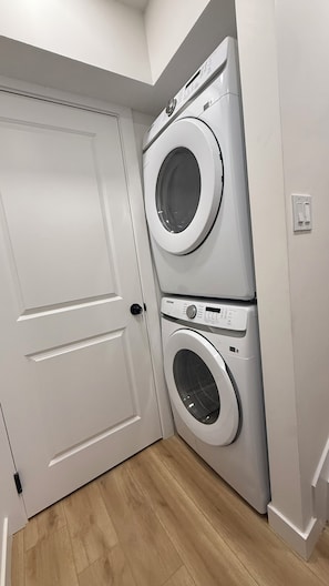 A laundry room with two stacked washing machines, a white door, and a light switch on the wall. - Our Cozy Corner (Edmonton)