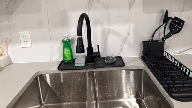 Une cuisine dotée d’un évier en acier inoxydable, de meubles de rangement en bois, d’un robinet noir et d’un porte-ustensiles noir.