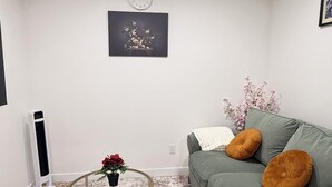 Un salon avec un canapé vert, deux petites tables rondes, une horloge murale et un tableau encadré.