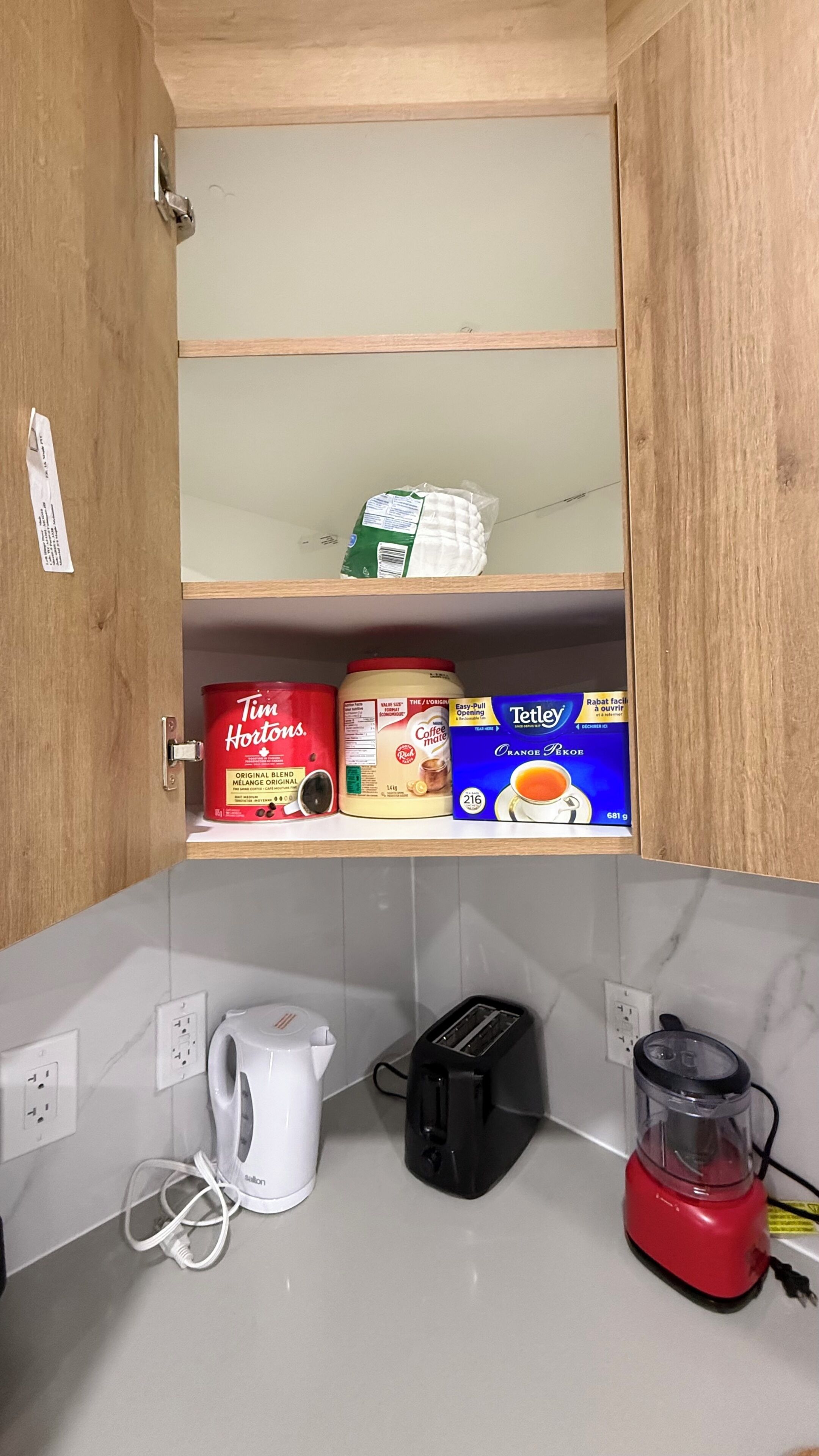 Una cucina con macchina da caffè, tostapane, frullatore e un armadietto contenente caffè e tè.
