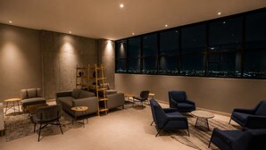 En moderne lounge med sofaer, stole, en træstige og udsigt over byen gennem store vinduer.