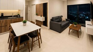 Un appartement moderne comprenant une cuisine, un coin repas, un salon et une grande fenêtre donnant sur la ville.