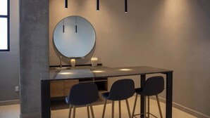 Un espace repas moderne agrémenté d’un miroir rond, de trois chaises, d’une table rectangulaire et de luminaires suspendus.