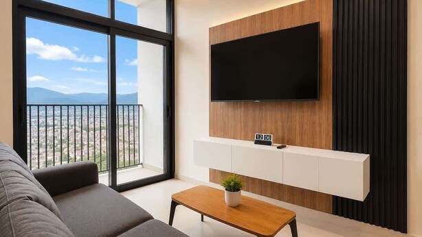 Un salon moderne doté d’une grande fenêtre, d’un téléviseur à écran plat fixé au mur, d’un canapé et d’une table basse.
