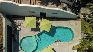 An aerial view of a swimming pool with a unique shape, surrounded by umbrellas and palm trees. - Just a few steps from Arrocito Beach, with amenities, a pool, internet, and parking. (Santa María Huatulco)