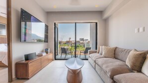 A modern living room with a sofa, a coffee table, a TV mounted on the wall, and a sliding glass door leading to an outdoor patio. - Modern Versalles 2BR w/ Rooftop Pool & Views in Puerto Vallarta (Puerto Vallarta)