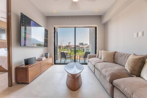 A modern living room with a sofa, a coffee table, a TV mounted on the wall, and a sliding glass door leading to an outdoor patio. - Modern Versalles 2BR w/ Rooftop Pool & Views in Puerto Vallarta (Puerto Vallarta)