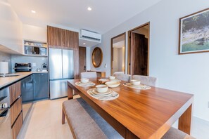 A modern kitchen with built-in appliances, a dining area with a wooden table set for four, and a view of a tropical landscape through an open door. - Modern Versalles 2BR w/ Rooftop Pool & Views in Puerto Vallarta (Puerto Vallarta)
