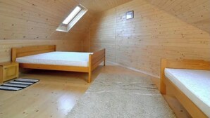 A small, wooden-paneled room with a sloped ceiling, a single bed, a window, and a small desk.