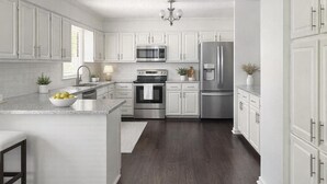 A modern kitchen with white cabinetry, stainless steel appliances, and a dark wood floor. - 3 Bedroom Backyard Oasis Near FIFA World Cup Events (Blue Springs)
