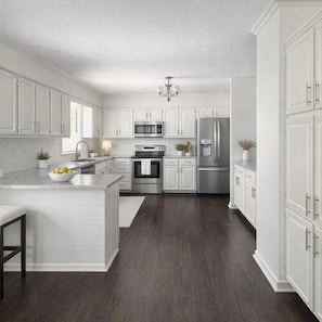 Una cocina moderna con armarios blancos, electrodomésticos de acero inoxidable y piso de madera oscura.
