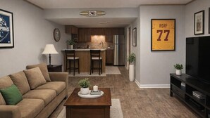 A living room with a sofa, coffee table, TV, kitchen area, and a framed sports jersey on the wall. - 3 Bedroom Backyard Oasis Near FIFA World Cup Events (Blue Springs)