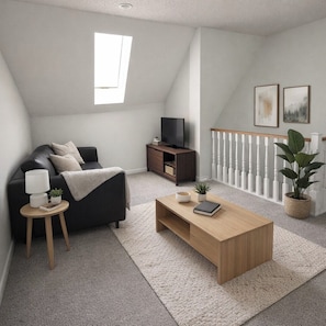 A modern loft bedroom with a sloped ceiling, a large window, a dark sofa, a wooden coffee table, a small side table, a TV on a wooden stand, and a white railing. - 3 Bedroom Backyard Oasis Near FIFA World Cup Events (Blue Springs)