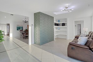 Ein modernes Wohnzimmer mit einem braunen Ledersofa, einem Essbereich mit einer Chandelüster und einer Wand aus Ziegelsteinen.