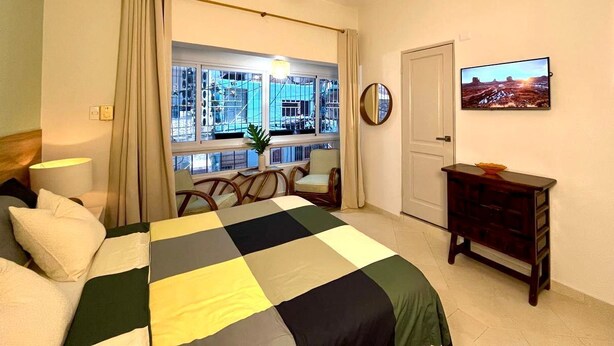Quarto de hotel com cama, janela vista para a cidade, ventoinha no teto e cômoda.