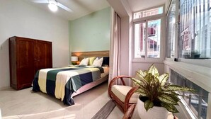 Quarto com cama, guarda-roupa de madeira, uma cadeira, planta em vaso e janela com vista.