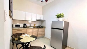 Cozinha compacta com armários brancos, geladeira de aço inoxidável, micro-ondas e uma pequena mesa de jantar com cadeiras.