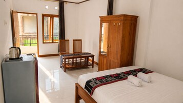 A bedroom with a bed, a wooden wardrobe, a desk with a kettle, and a chair.