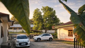 A white car parked in a driveway with a house in the background. - Ocha Bajo Homestay (Labuan Bajo)