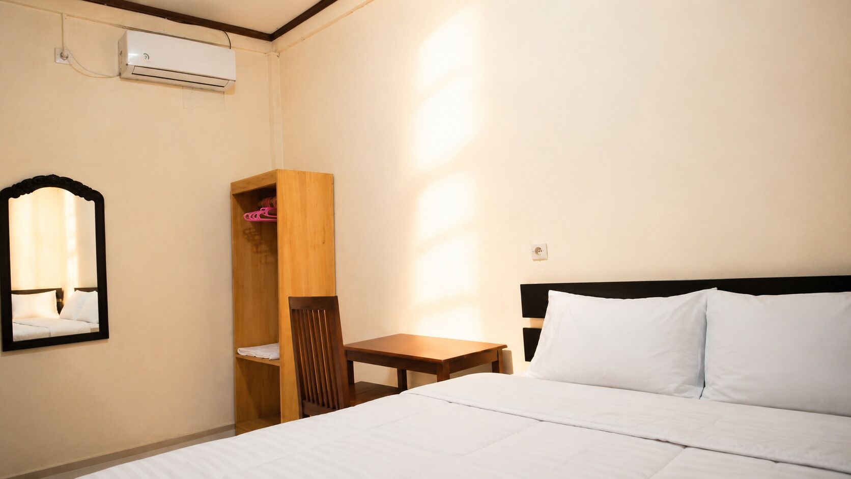 Une chambre d’hôtel comprenant un lit, une table de chevet en bois, une chaise, un miroir et une armoire.