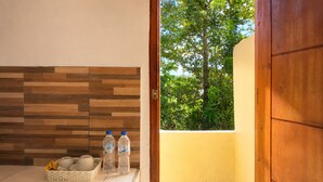 A bathroom with a wooden wall, a window with a view of trees, and a basket with toiletries. - Ocha Bajo Homestay (Labuan Bajo)