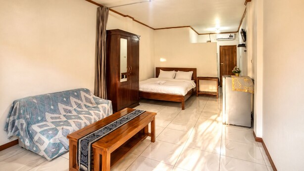 A bedroom with a bed, a wooden bench, a wardrobe, and a refrigerator. - Ocha Bajo Homestay (Labuan Bajo)
