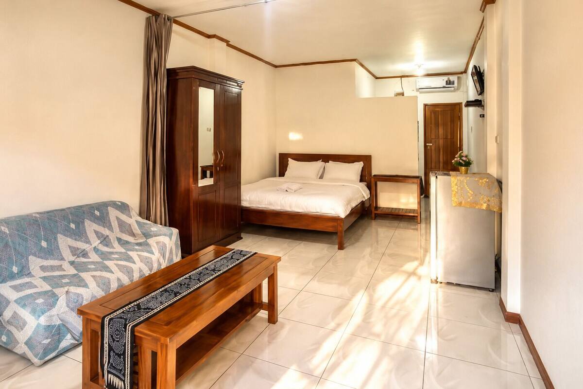 A bedroom with a bed, a wooden bench, a wardrobe, and a refrigerator.