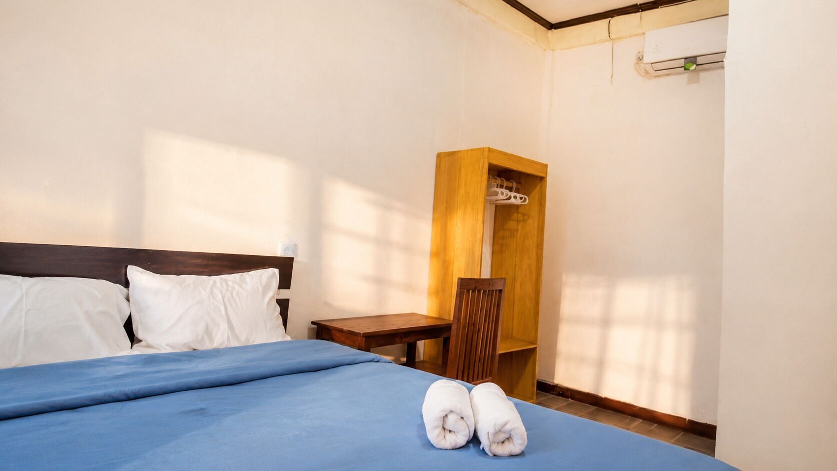 A hotel room with a bed, a wooden nightstand, a chair, and a wardrobe.