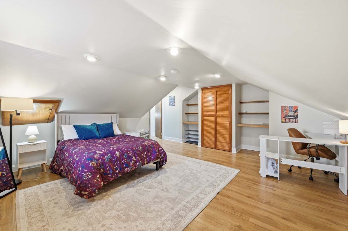 A bedroom with a bed, a desk, a chair, a lamp, a wardrobe, and a shelf.