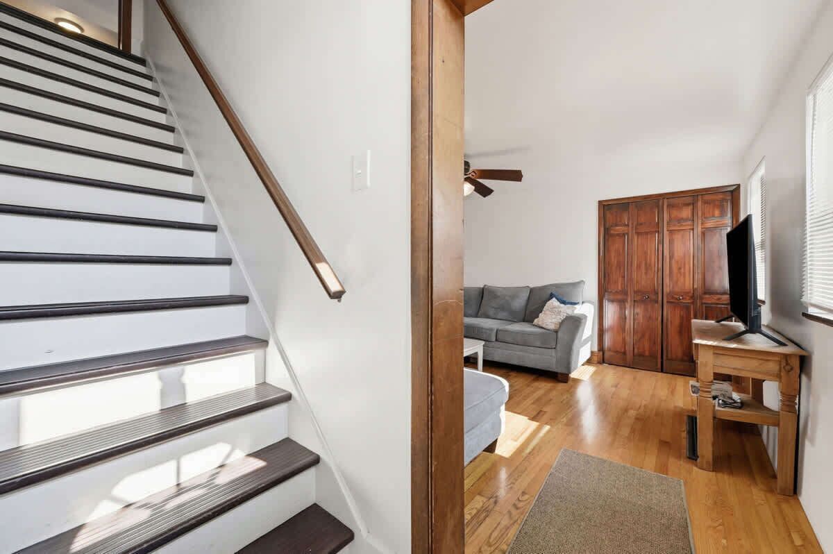 A staircase with wooden handrails and a grey sofa in a living area with wooden flooring and a television.
