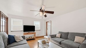 Ein modernes Wohnzimmer mit Flachbildfernseher, zwei grauen Sofas, einem Couchtisch und einem Deckenventilator.