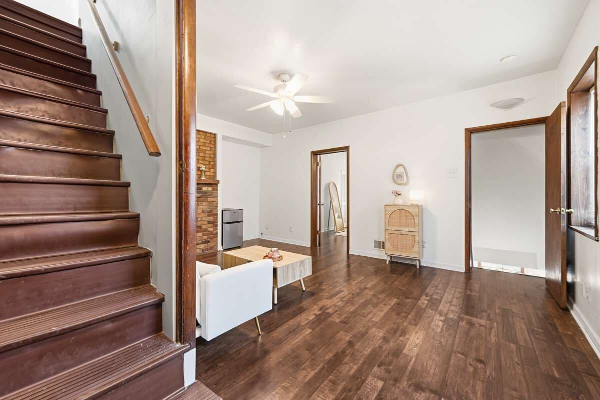 A spacious living area with a wooden staircase, a ceiling fan, a dining table, and a kitchen area.
