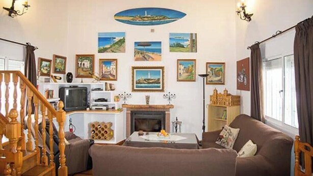 Een woonkamer met een open haard, een televisie, een trap en een verzameling ingelijste foto's aan de muur.