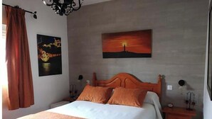 Een slaapkamer met een bed, een nachtkastje, een aan de muur hangend schilderij en een raam met gordijnen.