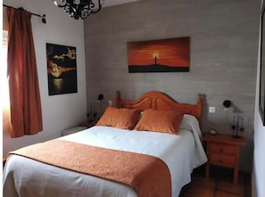 Ein Schlafzimmer mit einem Bett, einem Nachttisch, einem Wandbild und einem Fenster mit Vorhängen.