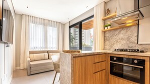 Uma cozinha moderna com forno embutido, um espaço de refeições com sofá e vista para um edifício residencial.