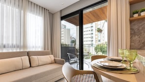 Uma sala de estar moderna com sofá, mesa de jantar e cadeiras, uma varanda com vista para edifícios e teto de madeira.