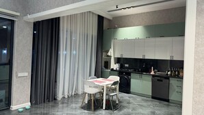A modern kitchen with white cabinets, a dining table with chairs, and a large window with curtains. - Villa warm pool (Баку)